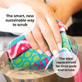 A hand cleans a metal pot under running water with a colorful Skoy Scrub: Good Clean Fun! pad by Skoy Enterprises, shown as a smart, sustainable alternative to traditional pads.