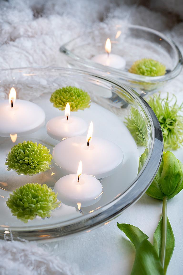 Floating white 2" Floater Tealight candles and green flowers in clear glass bowls create a cozy atmosphere, complemented by a green tulip on a white background.