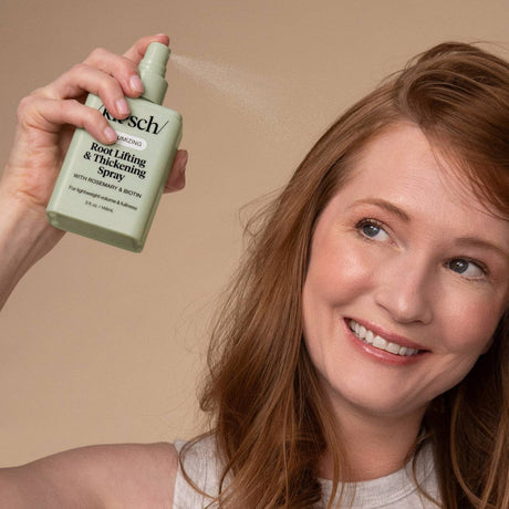 A woman smiles as she sprays Kitsch Hair: Root Lifting & Thickening Spray 5 fl oz near her scalp for added volume.