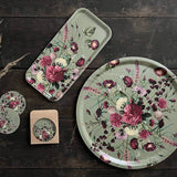 Tray and coasters made from Nordic birch veneer, decorated with pink, purple, and white flowers on green, displayed on a dark wood surface next to dried grass.