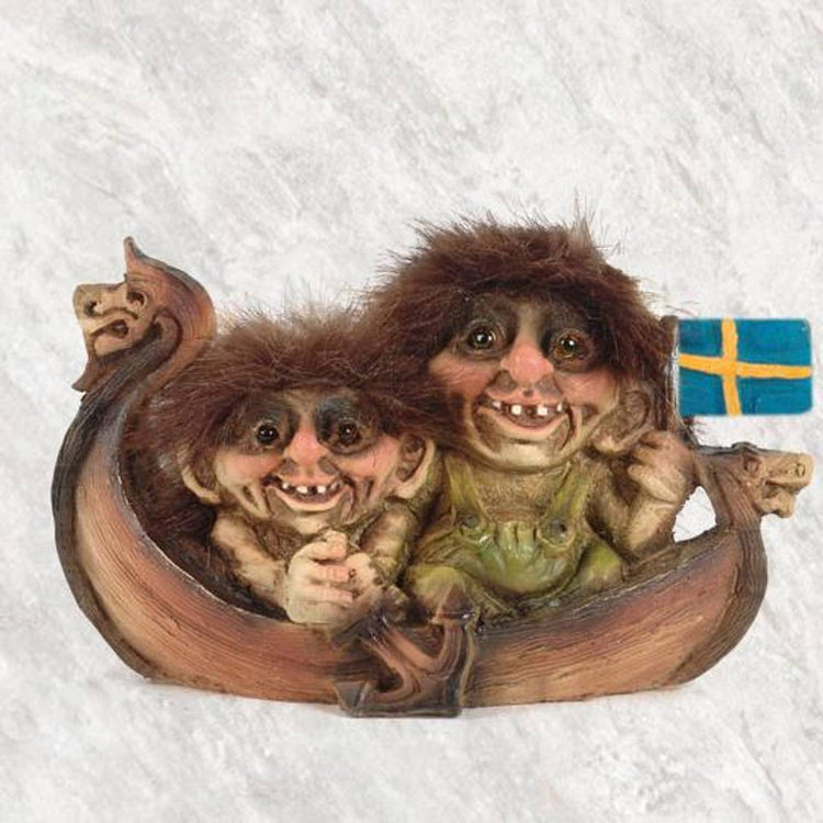 A pair of NyForm troll figurines with fuzzy hair are seated in a small wooden Viking ship, with one proudly holding a Swedish flag, highlighting aspects of playful Norwegian design.