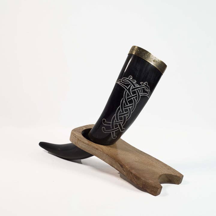 The Horn: Viking Drinking Horn Odin's Ravens with silver Celtic designs and a gold rim, beautifully displayed on a wooden stand, brings to mind the essence of Odin's Ravens.