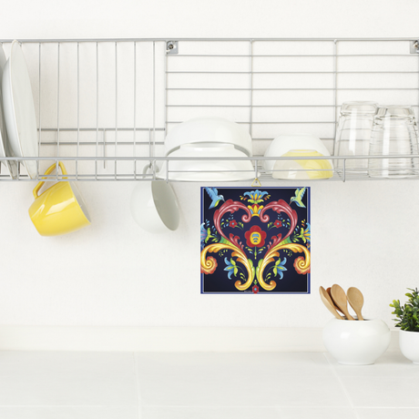 A metal dish rack with plates, cups, and glasses is mounted above a kitchen counter. Below it hangs the Blue Norwegian Rosemaling Ceramic Wall Decor 6 Square Tile with a colorful floral and heart pattern.