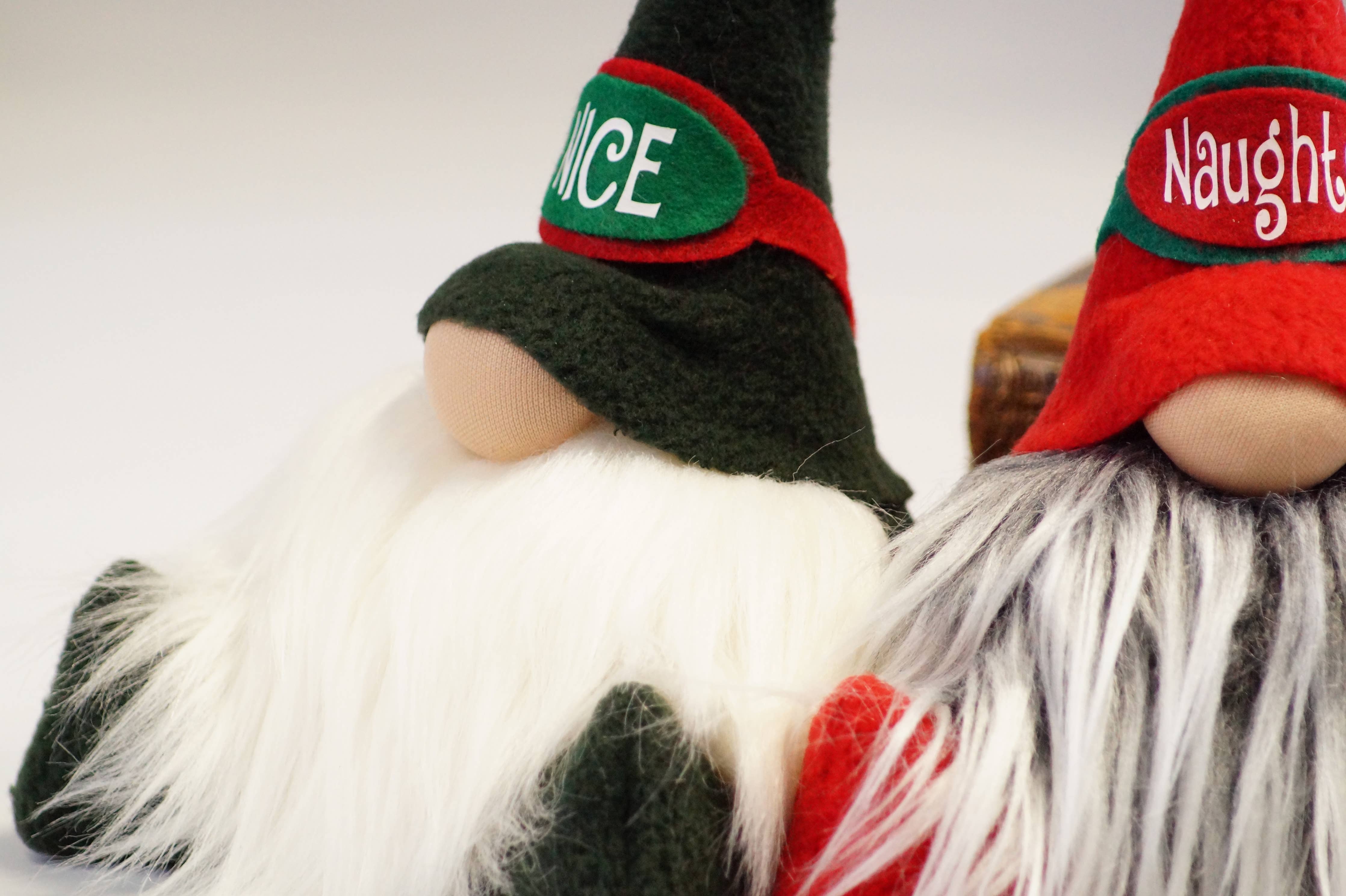 Two handmade plush gnome figurines with white beards are on display. The one on the left, known as the "Nice Christmas Gnome," is adorned with a green hat featuring the word "Nice," making it an ideal addition to your festive Christmas décor. The gnome on the right wears a red hat emblazoned with "Naughty.