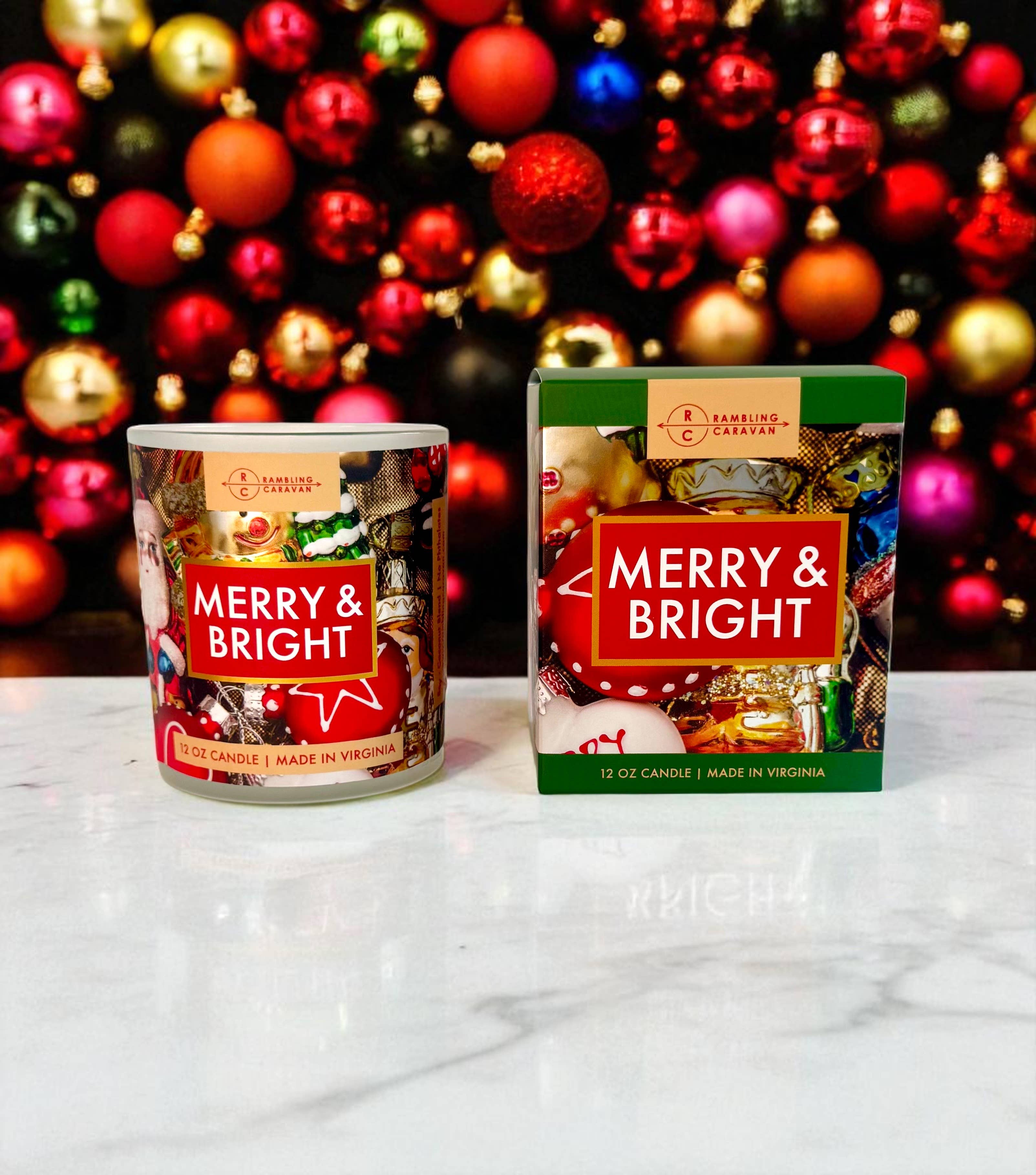 A Merry & Bright Candle 12oz and its box are displayed on a marble surface with festive ornaments, highlighting this premium holiday candle—ideal for adding a cheerful touch to your seasonal decor.