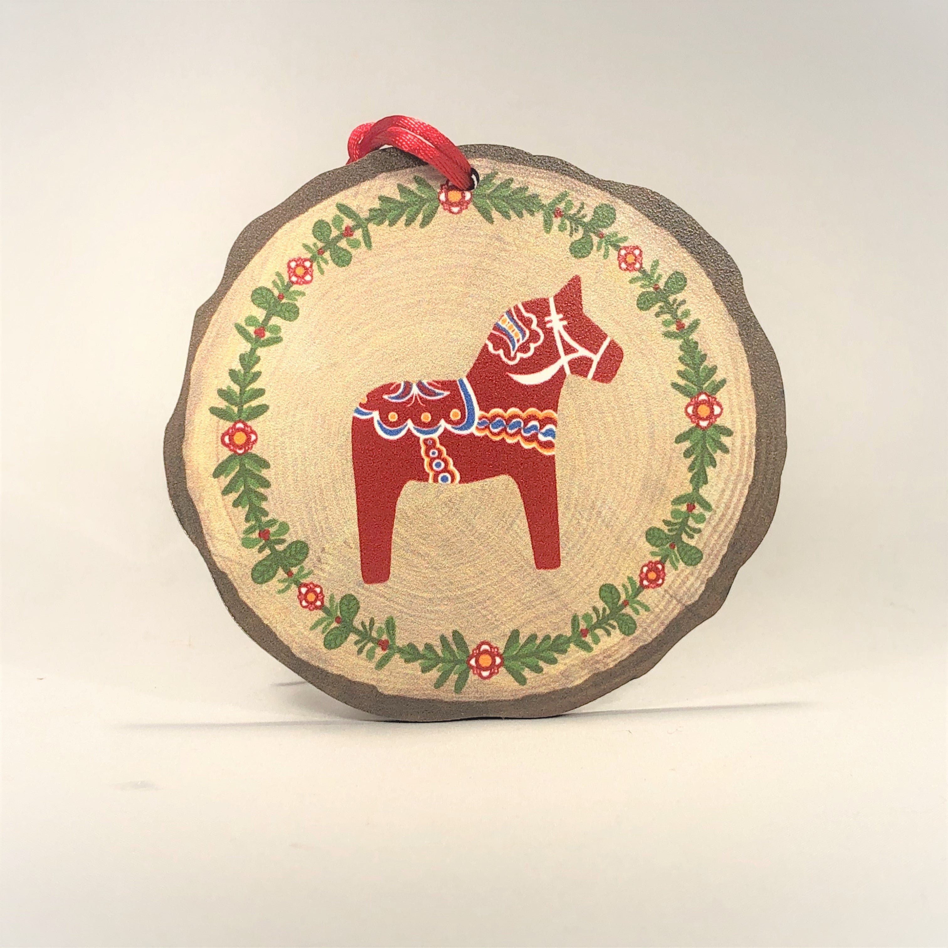 The Ornament: Dala Horse - Red with Kurbits and Wreath (3 5/8" diameter) features a red and blue Swedish Dala Horse at the center, surrounded by a green and red floral wreath and topped with a red ribbon—a charming Nordic accent.