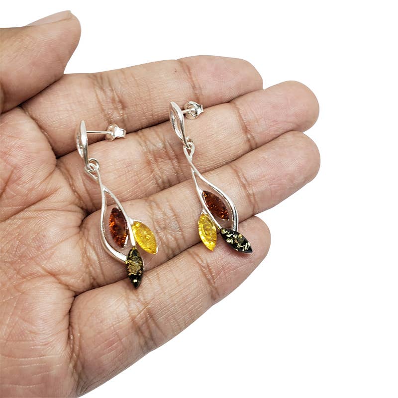 A hand holds sterling silver earrings, featuring a marquise shape with three Baltic amber stones in amber and yellow shades.