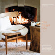 A wooden chair with a white cushion and sheepskin sits by the fire; a rustic table holds coffee, snacks, and the book "The Hygge Life" by Karl Gislason & Jody Eddy. Cozy recipes set the mood. Text reads: the hygge life.