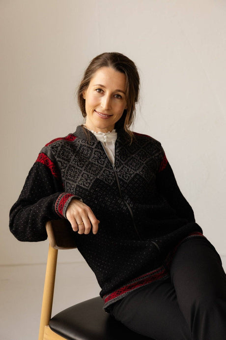 Woman wearing a zip-up Norwegian wool cardigan with a gray and red Nordic geometric pattern on the shoulders and cuffs and a fleece-lined collar.