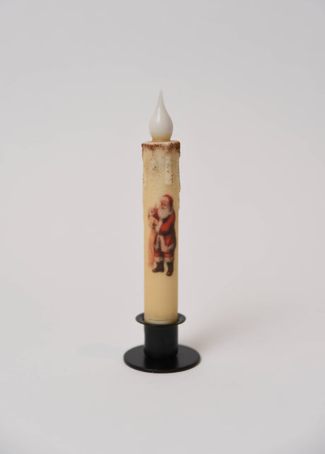 Cream-colored LED taper candle with a Santa Claus graphic, set in a black stand.