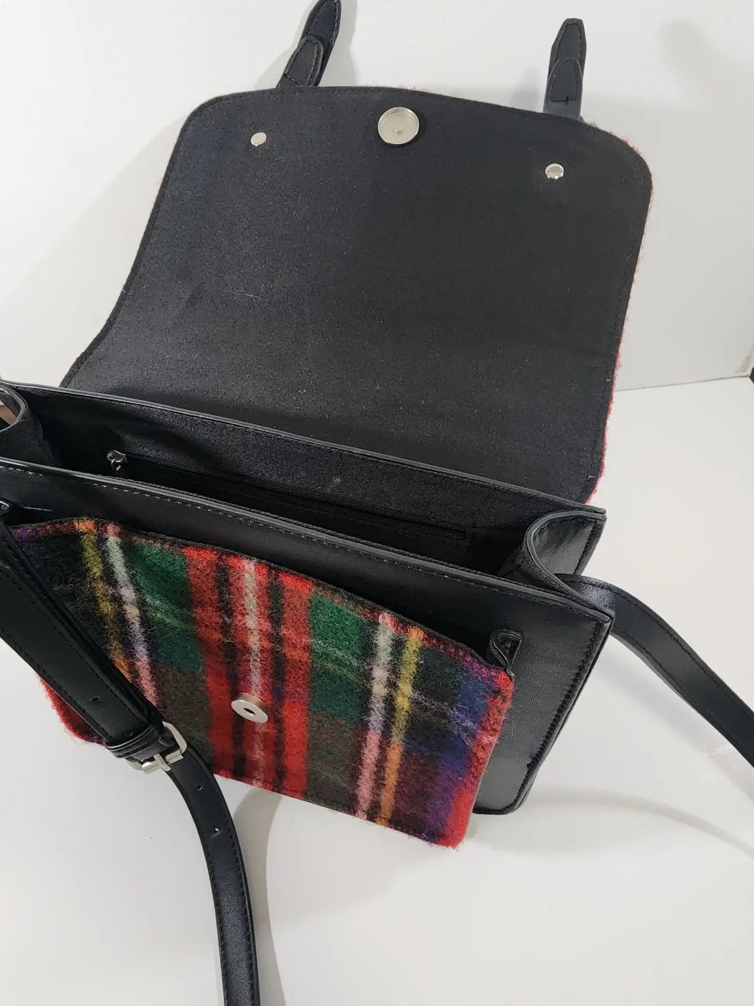 The Bag: Royal Stewart Handbag is a black wool bag with an open flap, showing a front pocket lined in classic Scottish tartan featuring red, green, and yellow plaid accents.