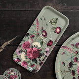 Nordic birch veneer tray decorated with pink, purple, and white flowers on a dark wooden surface next to two matching floral circular plates.