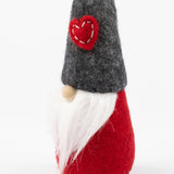 Scandinavian gnome figurine with a white beard, red wool felt body, gray felt hat, and a stitched red heart patch on the front of the hat.