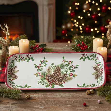 A tray with pinecone and holly design on a wooden table, surrounded by candles, greenery, ornaments, and a lit Christmas tree in the background.