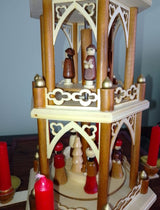 A wooden Christmas pyramid, made in Germany, features Pyramiden-Kerzen candle holders and includes a box of 50 red Christmas Pyramid Candles (14 x 70mm) with carved figures on two tiers around a central tree.