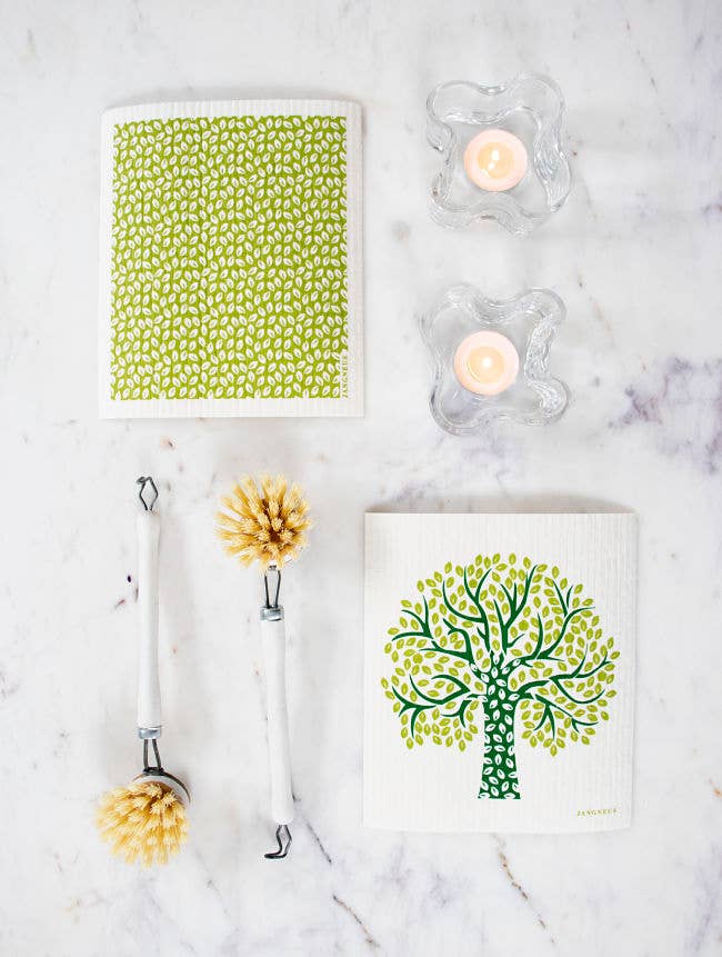 A Dish Cloth: Tree - Green, featuring a tree design, sits alongside two brushes and two lit candles on a marble surface, infusing the kitchen with a touch of Scandinavian style.