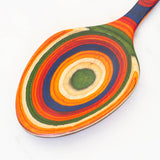 Serving spoon with handle and bowl decorated with concentric circles in red, orange, blue, green, and yellow.