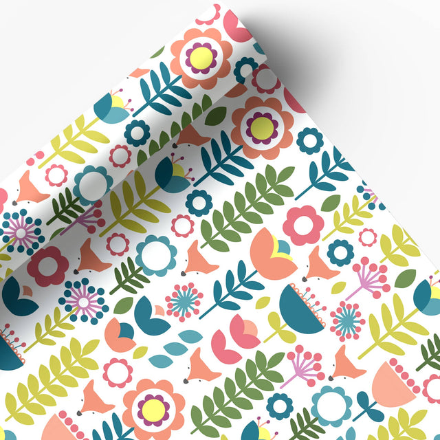 Juniper Blue’s "Tuli" Scandinavian Floral Folk Art Gift Wrap features cheerful pink, yellow, blue, and green flowers on glossy white paper. Includes 2 sheets (20"x29" each), partially unrolled to highlight the modern design.