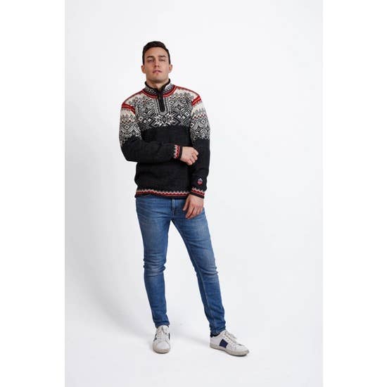 A man dressed in the Narvik Ski Sweater (312) in charcoal, crafted from 100% wool, is paired with blue jeans and sneakers as he stands against a white background.