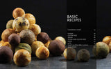 A stack of golden Danish pancakes (aebleskiver) rests on a dark surface next to the book Aebleskiver by Pim Pauline Overgaard: A New Take on Traditional Danish Pancakes, open to its recipe index.