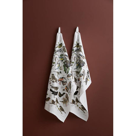 Two 100% organic cotton Garden Birds tea towels (19x27) by Carl Christian Tofte for Koustrupco hang on hooks against a brown wall.