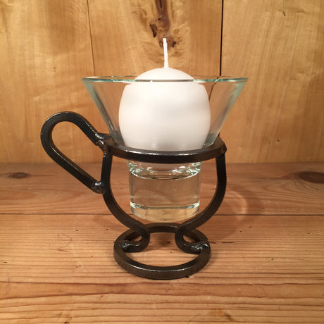The Danish Iron Coffee Cup candle holder, complete with a Leif glass cup nestled within its metal frame, evokes the spirit of Viking times as it sits gracefully on a wooden surface.
