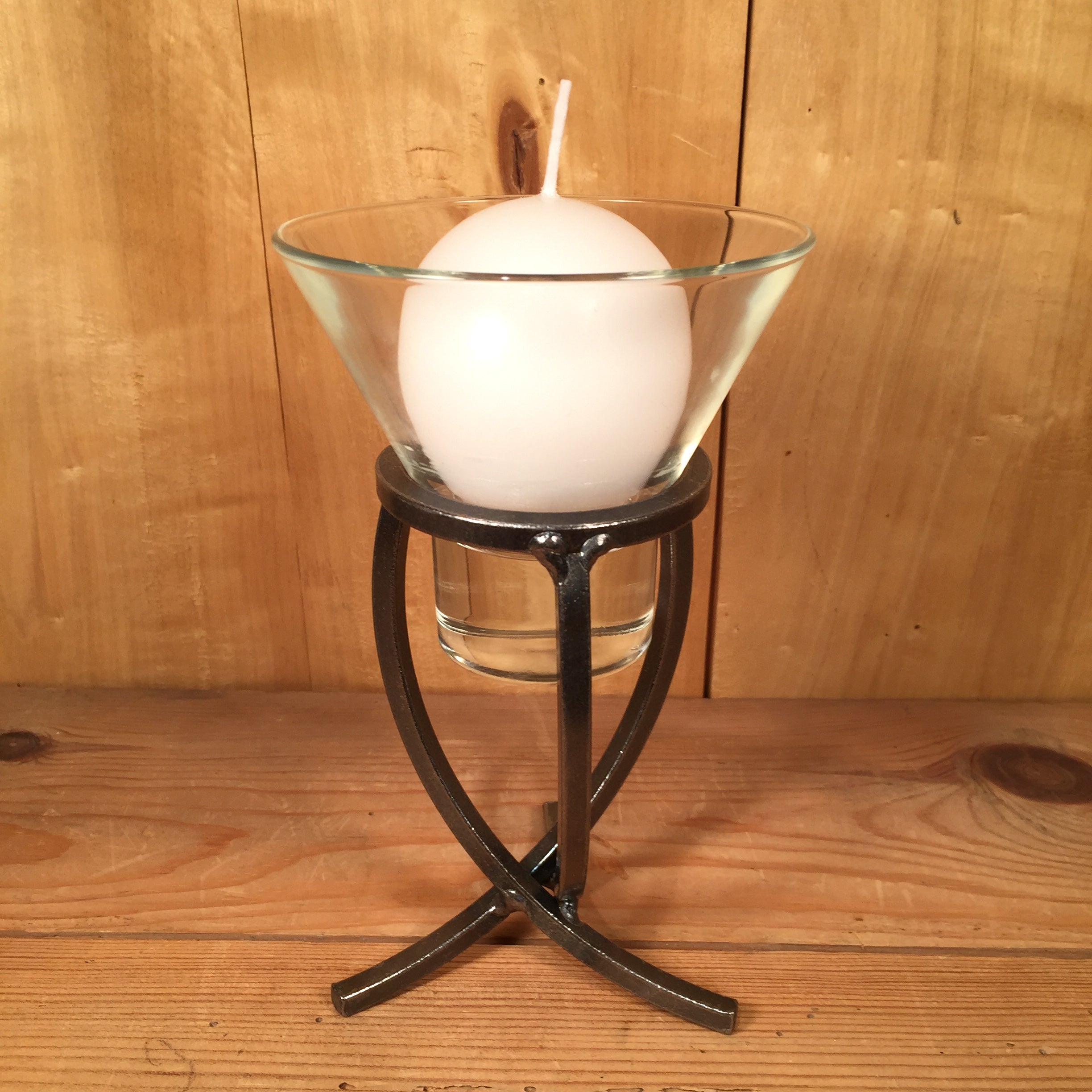 A white ball candle sits in a Leif cup on the sleek Danish Iron Candle Holder with a crossed iron base, all set against a rustic wooden backdrop.