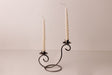 Two white spiral candles in a Danish iron holder with curved arms, set on a plain light surface with a neutral backdrop.