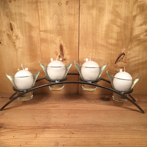 A set of four white candles in glass holders is elegantly arranged on the Danish Iron Arched Candle Holder for 4 Candles, creating a beautiful contrast against the wooden background.
