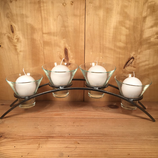 A set of four white candles in glass holders is elegantly arranged on the Danish Iron Arched Candle Holder for 4 Candles, creating a beautiful contrast against the wooden background.