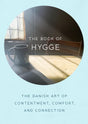 A book cover titled "Book: Book of Hygge, The Danish Art of Contentment, Comfort and Connection" encapsulates Danish happiness with a cozy home vibe, showcasing a mug on a sunlit table.