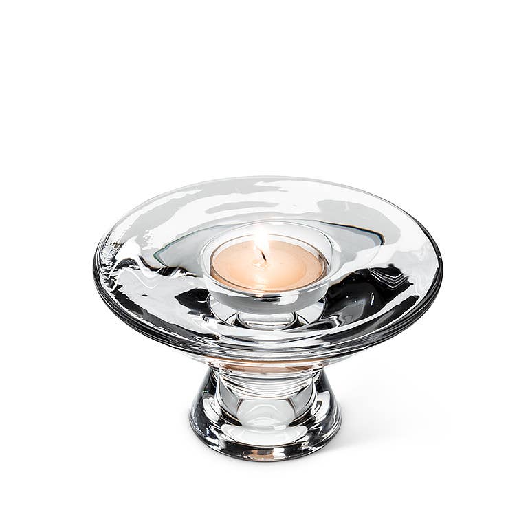 A lit tealight candle in the Reversible Glass Candleholder (4.5" D) showcases a clear design with a wide, flat top and a short, sturdy base.