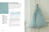 A light blue drawstring bag with white floral embroidery, inspired by Scandinavian design, hangs on a white door; the project is featured in Scandi Needlecraft: 35 Step-by-step Projects to Make by Clare Youngs (Paperback, 128 pages).