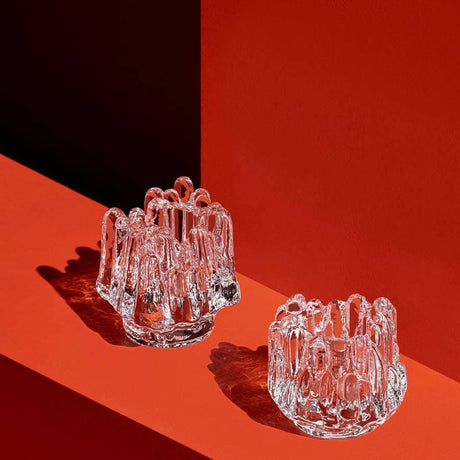 Two KostaBoda Polar Votive Clear Small sculptures (H-86mm x D-95mm), with irregular wavy edges, sit on a red surface against a red background.