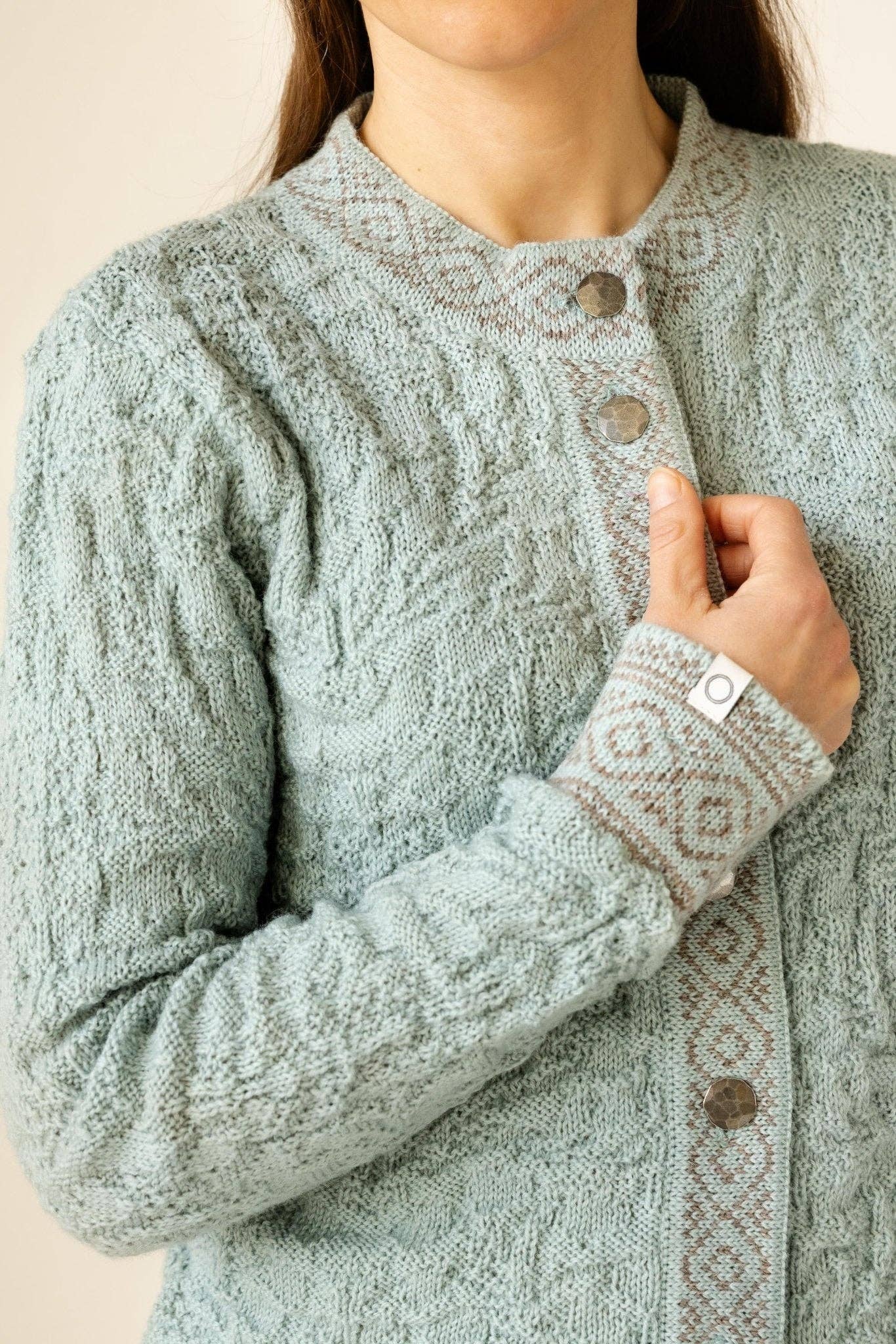 A person wearing the Bryggen Women's Norwegian Cardigan in white, featuring patterned trim and metal buttons; only the upper body is visible.