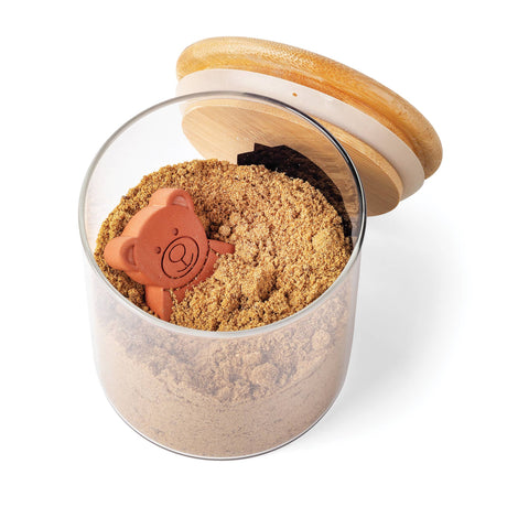 A glass jar holds brown sugar with the Sugar Saver: Terracotta Brown Sugar Bear Keeper & Saver, 2.5" nestled inside, and an open wooden lid resting beside it.