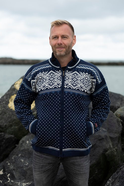 A person wearing the Norwegian Wind Blocker Navy Jacket made from 100% worsted wool stands outdoors with a rocky backdrop and water.