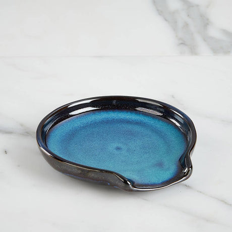 The Spoon Rest: Lake Life Ceramic Round Spoon Rest features a handmade design with a blue glazed center, dark rim, and pour spout. Crafted from food-safe ceramics, it combines style and function on your countertop.