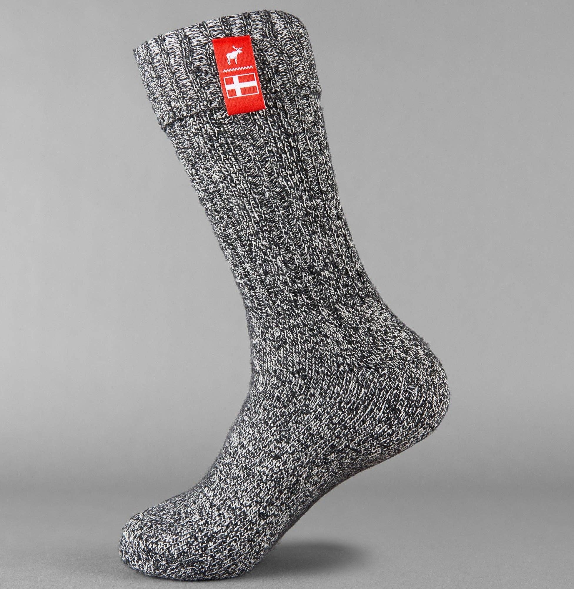 Embrace the Danish Hygge vibes with the Nordic Noir Danish Hygge Socks, featuring a gray wool design with a red tag showcasing a white deer and cross pattern. Perfect for staying warm during winter, these cozy socks effortlessly blend comfort and style.