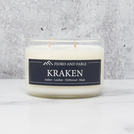 An 8oz white soy wax candle in a clear glass jar labeled Fjord & Fable Candle: Kraken, featuring scent notes of amber, sea salt, driftwood, and leather.