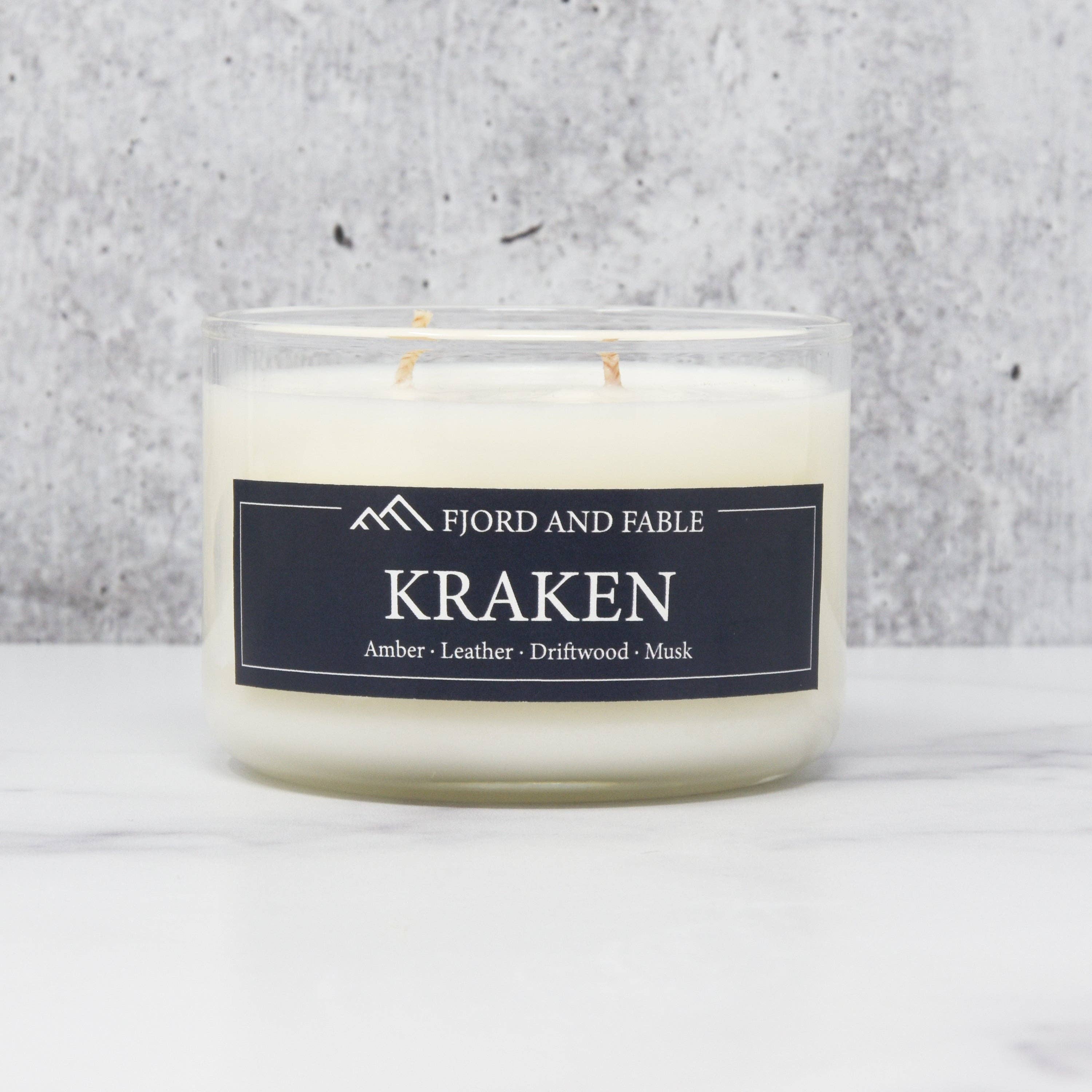 A Candle: Kraken Premium Soy Candle: 4oz by Fjord and Fable rests elegantly on a marble surface, filling the air with luxurious scents of amber, leather, driftwood, and musk. This vegan candle provides an exquisite aroma that captivates the senses.