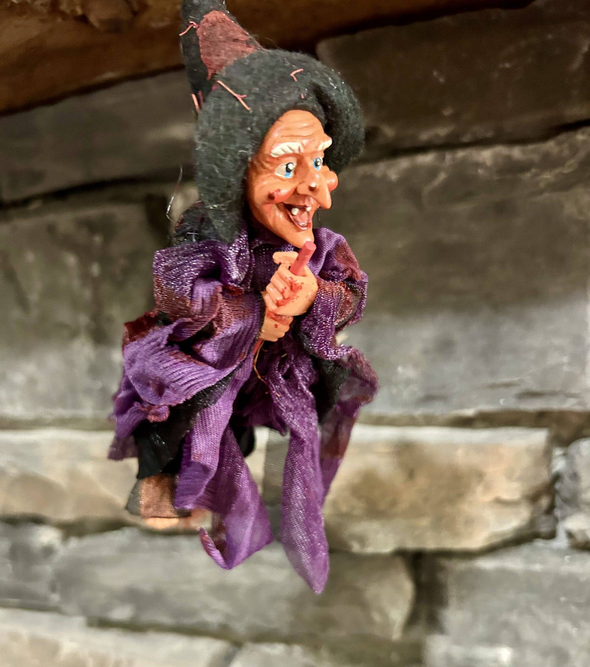 The Walburga Purple Kitchen Witch Doll is an 8" hanging broom rider figurine with a pointed hat, purple outfit, and mischievous smile—perfect as a whimsical good luck charm for kitchen protection.