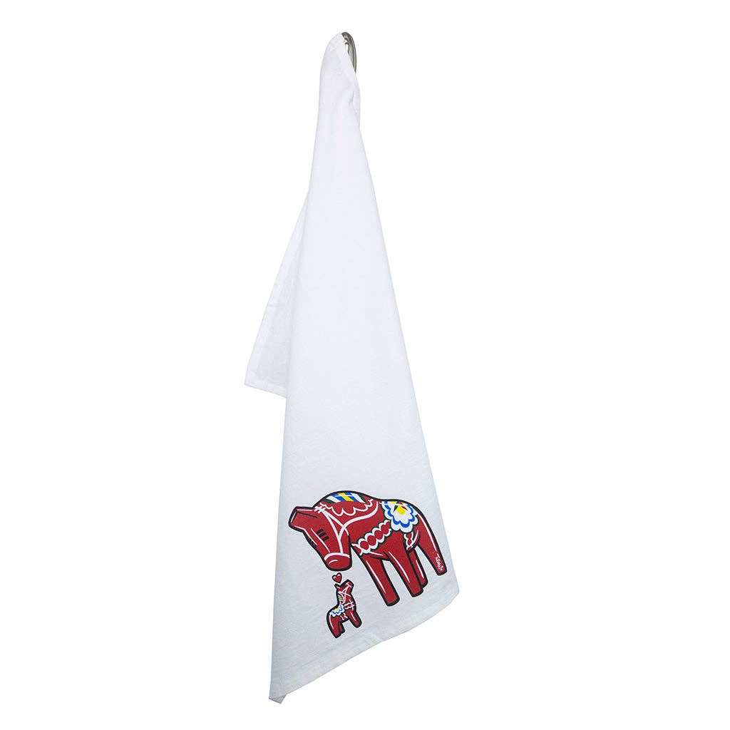 The Tea Towel - Dala Horse "Jumbo" by Adam Turman hangs on a hook, showcasing a large red Dala horse and a smaller matching horse with Swedish-style patterns—ideal for adding Scandinavian charm to your kitchen.