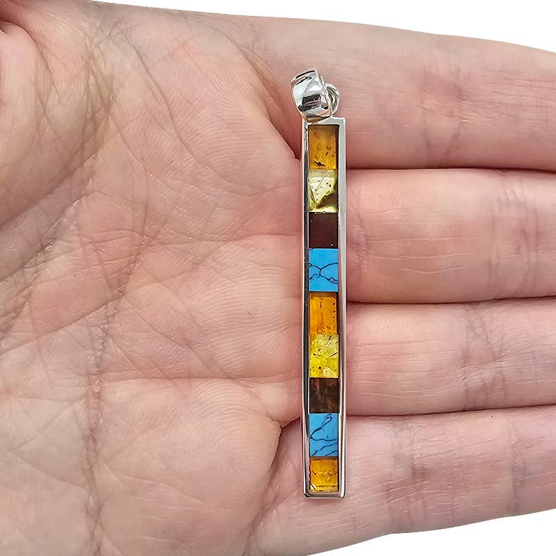 A hand holds a beautiful pendant featuring Baltic amber and pressed turquoise stones set in sterling silver, with six square segments.