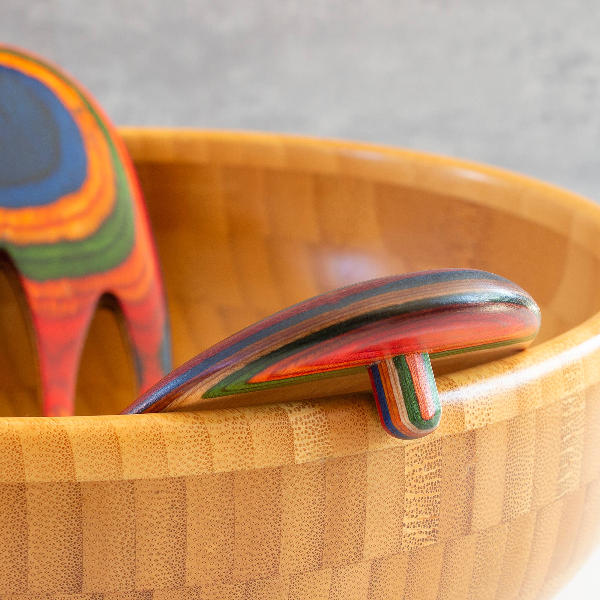 The vibrant Marrakesh Salad Hands rest on the edge of a bamboo bowl, making them perfect for tossing pasta salads.