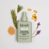 A bottle of Hair: Root Lifting & Thickening Spray 5 fl oz by Kitsch is displayed with rosemary, lavender, amber capsules, and granules on a light background, emphasizing this volumizing spray's botanical ingredients.