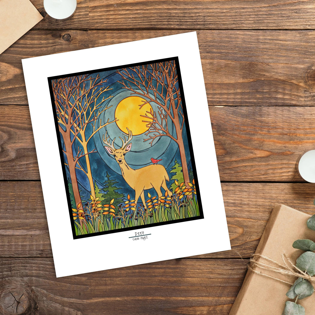Artwork titled "Deer" by Sarah Angst, a giclee print portraying a deer with antlers and a bird on its back in a forest beneath a full moon. The scene is enclosed by bare trees and wildflowers, created using high-quality pigmented inks.