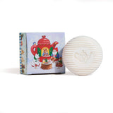 A round, white Gnome Soap Swedish Tea Bar with a teapot design is shown before its festive gift box, which is decorated with animals enjoying tea around a red teapot.