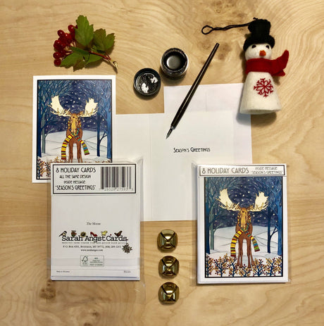 Card Pack: Holiday Moose Packaged Christmas Cards—8 cards with envelopes. Features a moose in snowy woods, bells, berries, and a felt snowman ornament. Envelope says Seasons Greetings. Made in USA for festive celebrations.