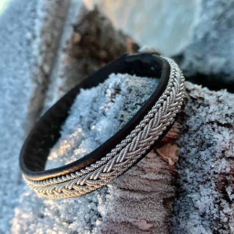 A handcrafted Traditional Sami Tennis Bracelet #2, 12mm wide with a dark brown band, rests on frost-covered wood. Made in Lapland, Sweden.